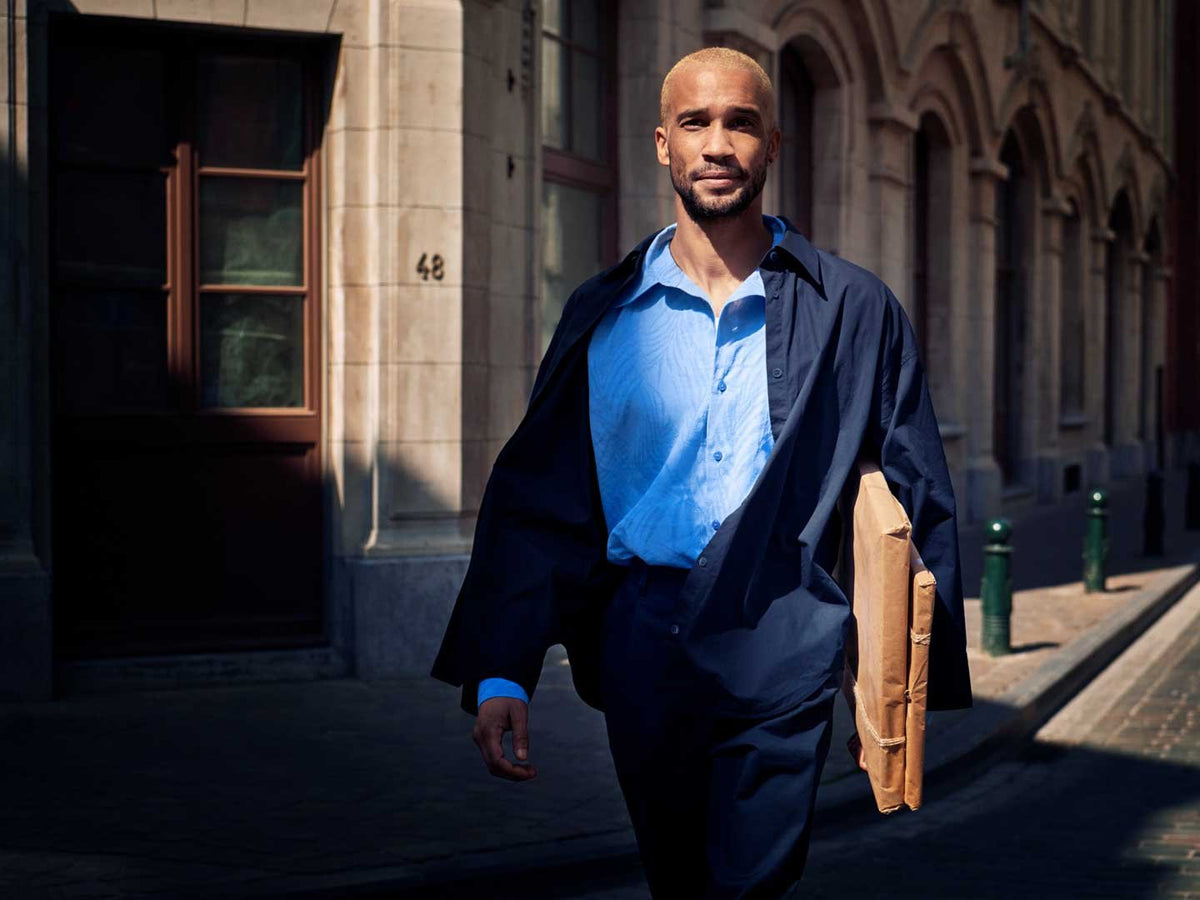 Mand i blå skjorte og mørk frakke går ad en gade