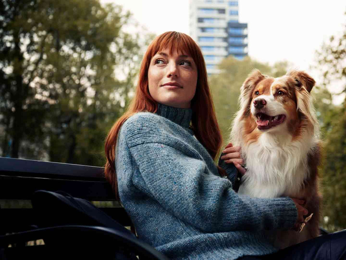 Kvinde i blå strikbluse sidder udenfor med sin hund