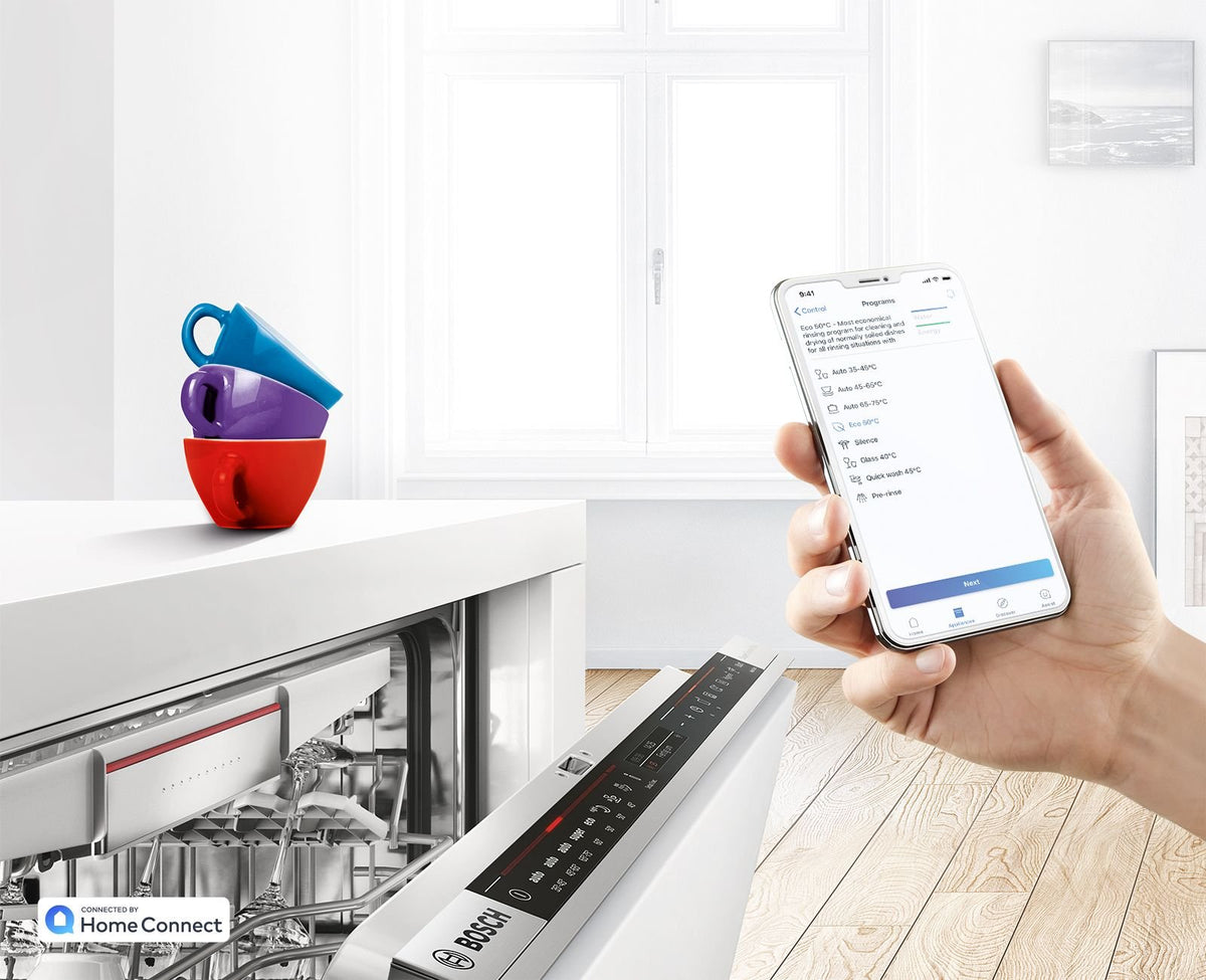Hånd med mobiltelefon og Home Connect-appen foran en åben Bosch opvaskemaskine