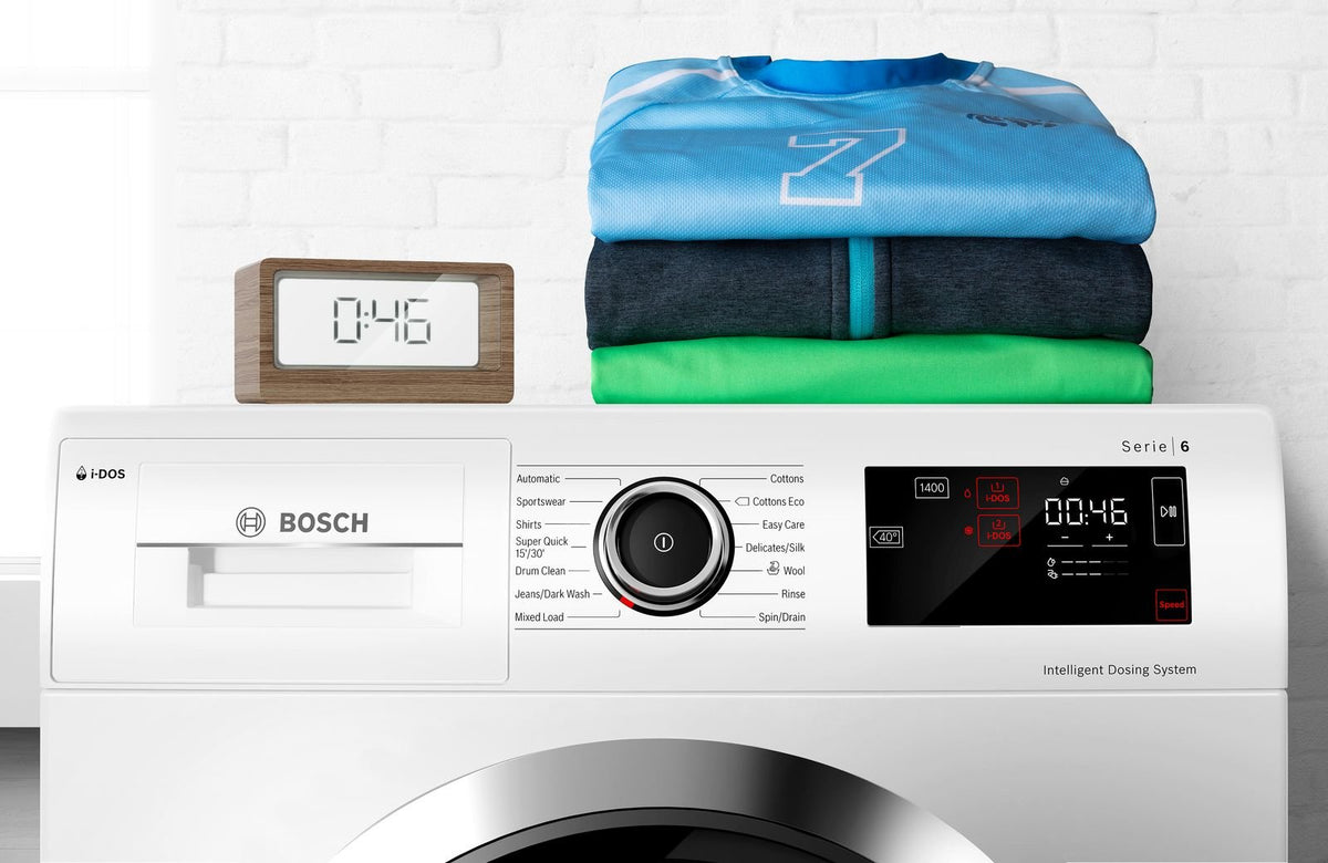 Bosch vaskemaskine med display og stak foldet tøj og et lille ur ovenpå