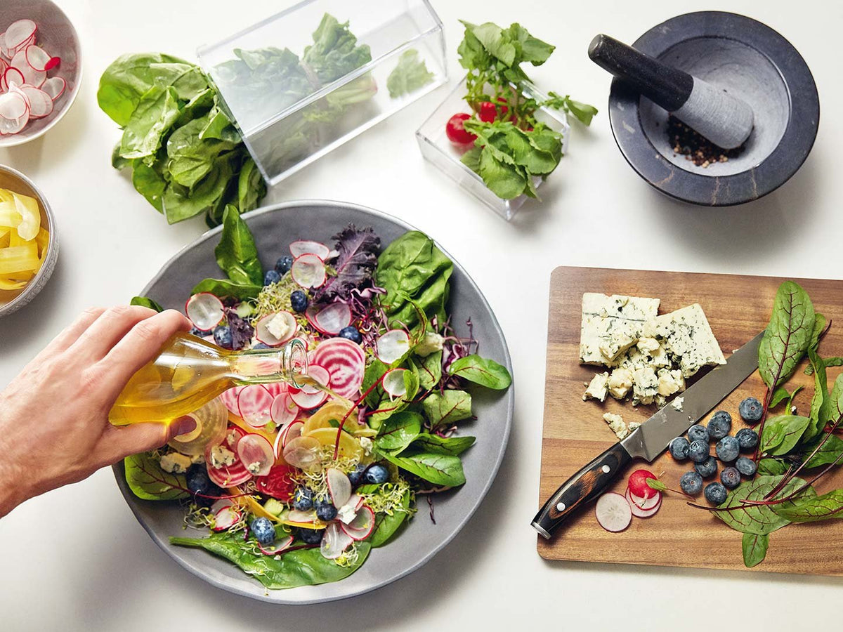 Hånd hælder olie over en salat med friske grøntsager