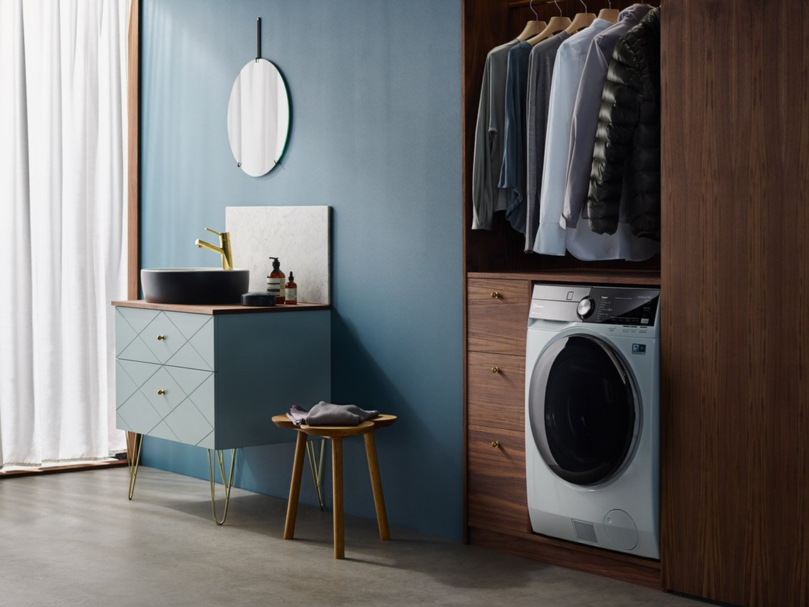 Electrolux vaske-tørremaskine i et blåt badeværelse med skjorter på bøjler