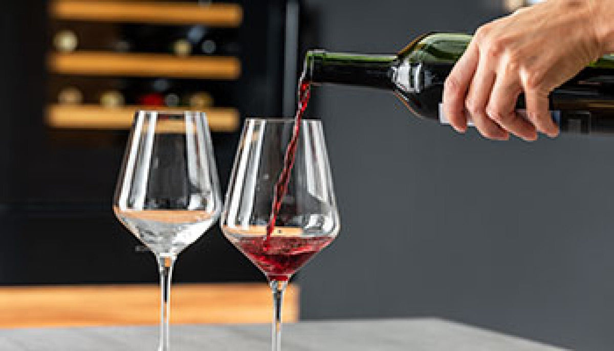 Rødvin skænkes i glas foran et Gram vinkøleskab