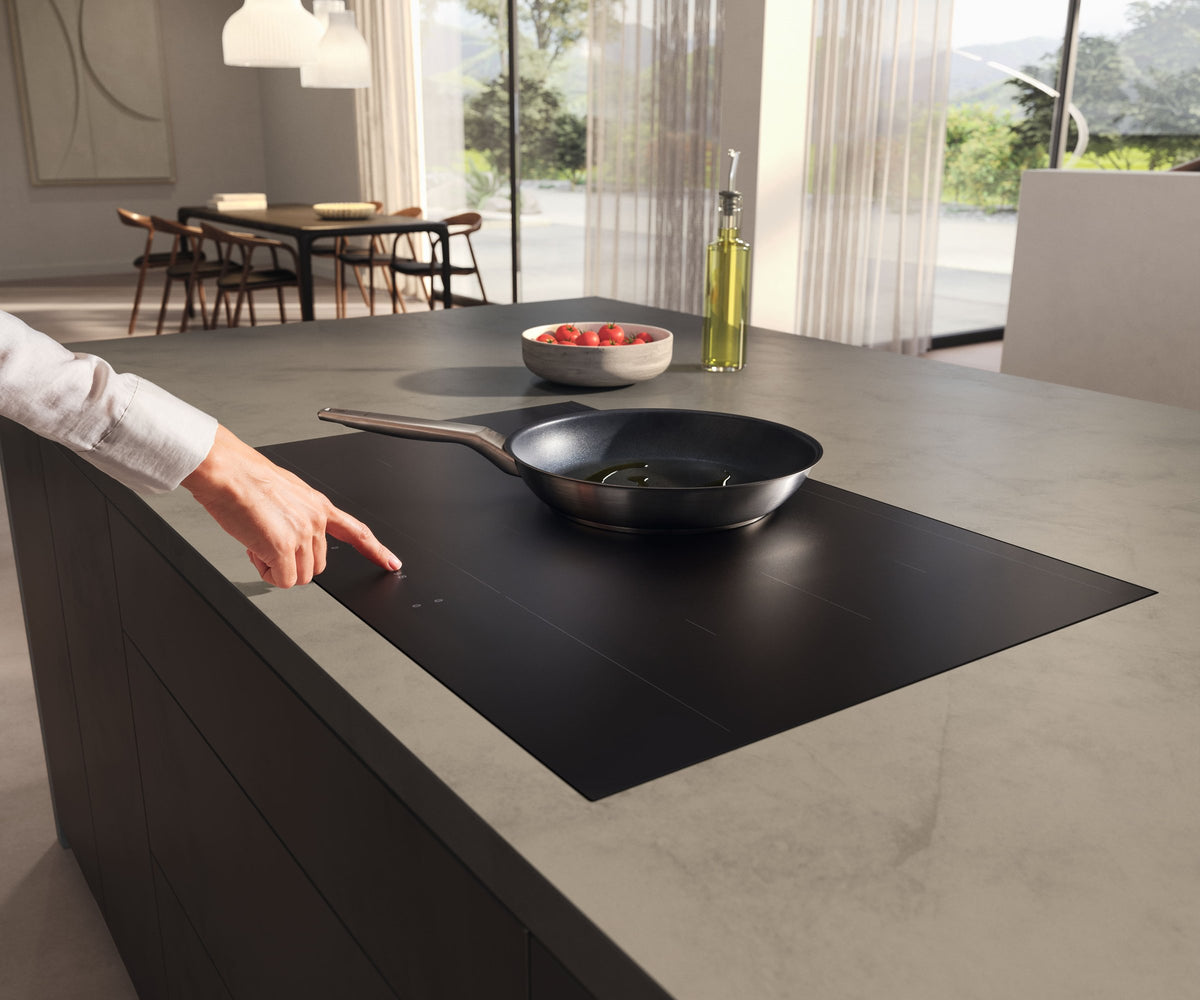 Person betjener en sort Miele induktionskogeplade med en pande i et lyst køkken