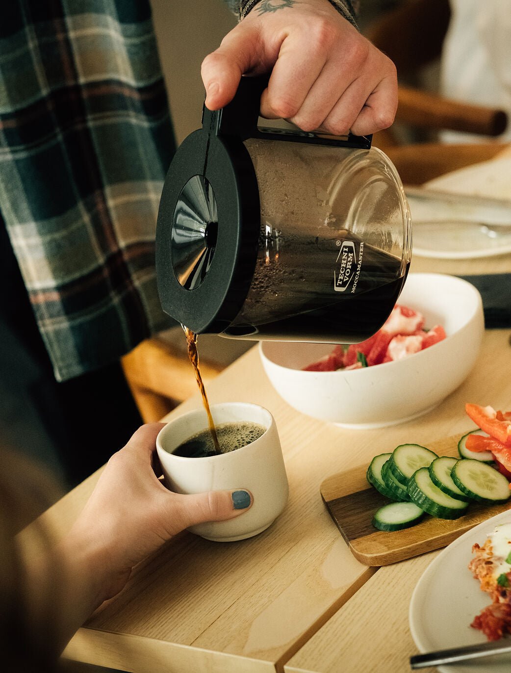 Hånd der hælder kaffe fra en Moccamaster glaskande i en kop