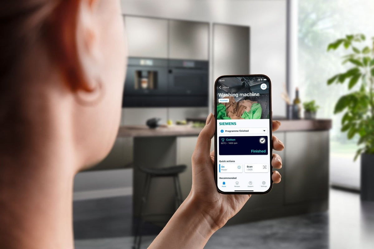 Person holder en mobil med Home Connect-appen foran en Siemens vaskemaskine