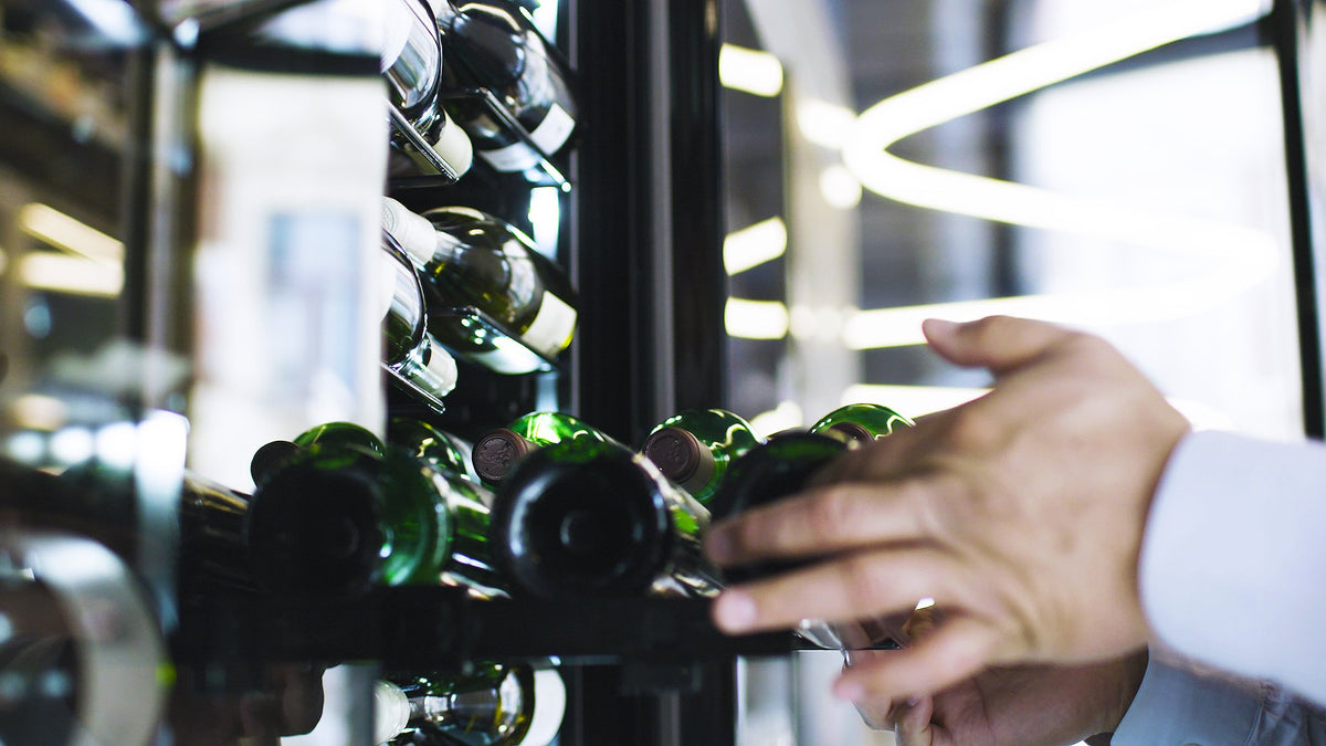 Hånd der tager en vinflaske fra en label view-hylde i et Temptech Copenhagen vinkøleskab